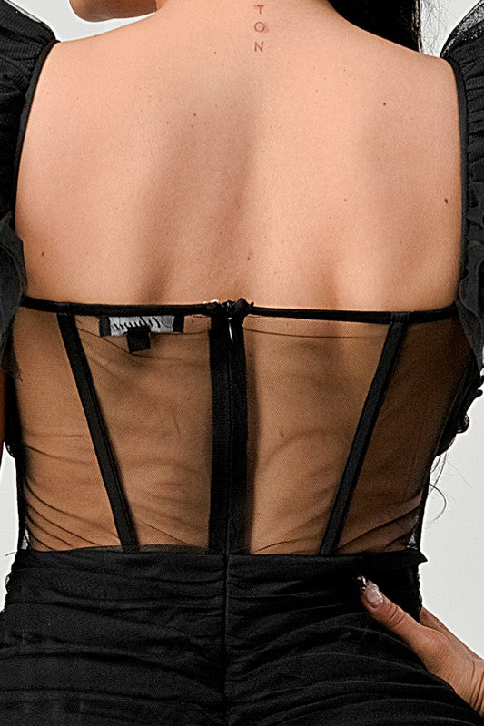 The dress is a chic black mini with a fitted silhouette, sheer paneling at the bodice, and dramatic ruffled cap sleeves that add a flirty, edgy touch