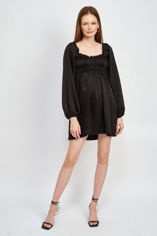 The dress is a black, long-sleeved mini with a smocked, square-neck bodice and a loose, flowy skirt that falls above the knees.