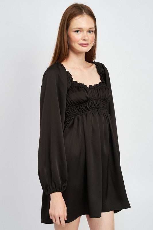 The dress is a black, long-sleeved mini with a smocked, square-neck bodice and a loose, flowy skirt that falls above the knees.