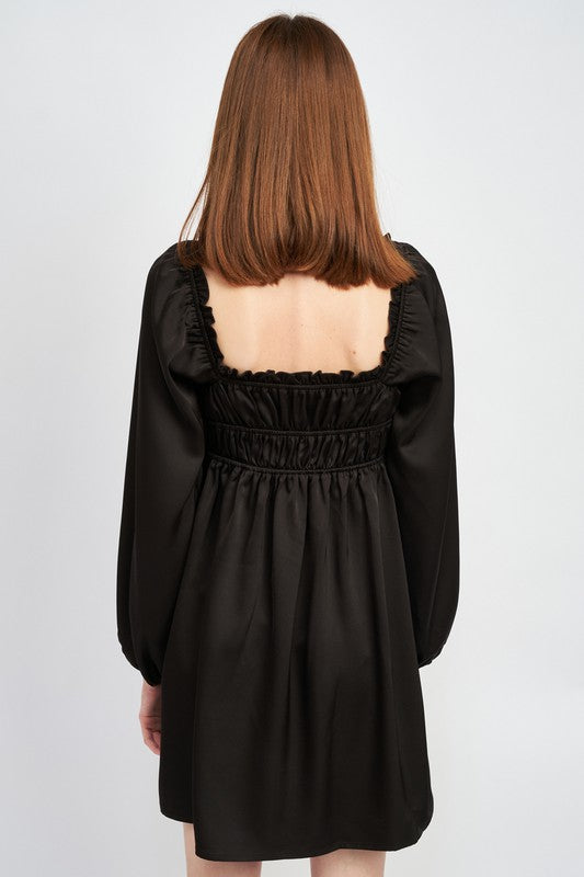 The dress is a black, long-sleeved mini with a smocked, square-neck bodice and a loose, flowy skirt that falls above the knees.
