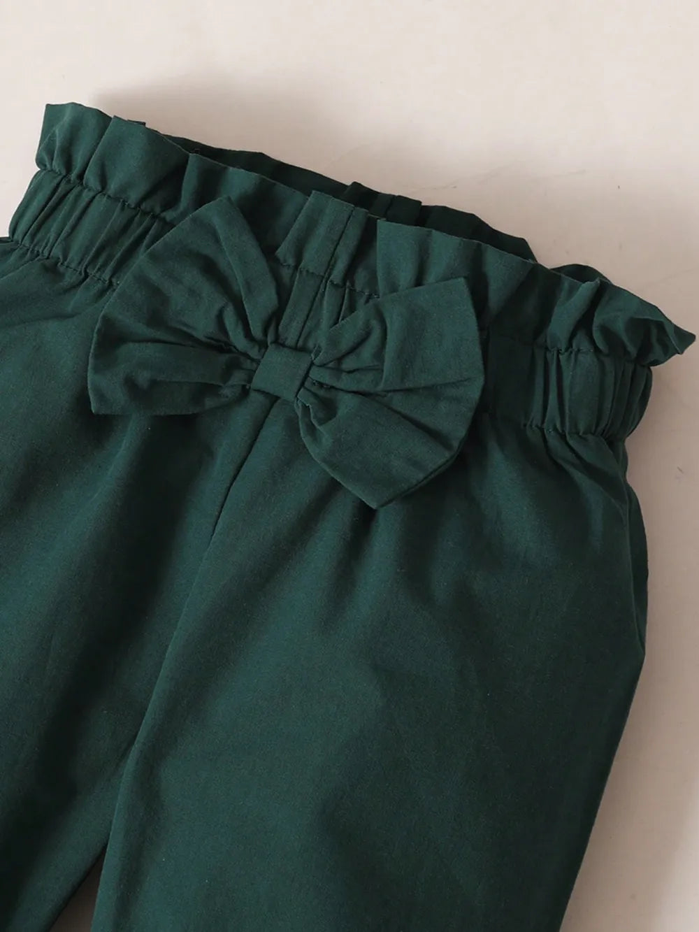 Baby girl two-piece outfit with white ruffled long-sleeve top and green bow accent, and matching green pants with coordinating bow detail