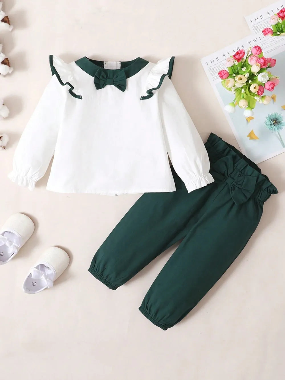 Baby girl two-piece outfit with white ruffled long-sleeve top and green bow accent, and matching green pants with coordinating bow detail