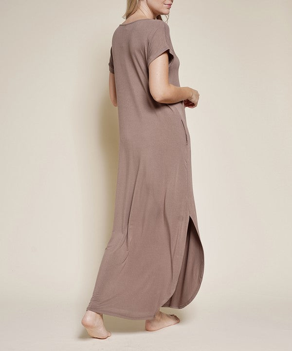 A woman wearing a grey maxi dress with short sleeves, barefoot, against a white background.
