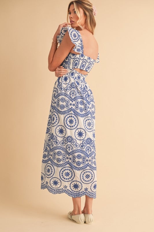 The dress is a long, airy maxi with a blue and white geometric/medallion print, cap sleeves, and a fitted bodice that flows into a relaxed, ankle-length skirt.