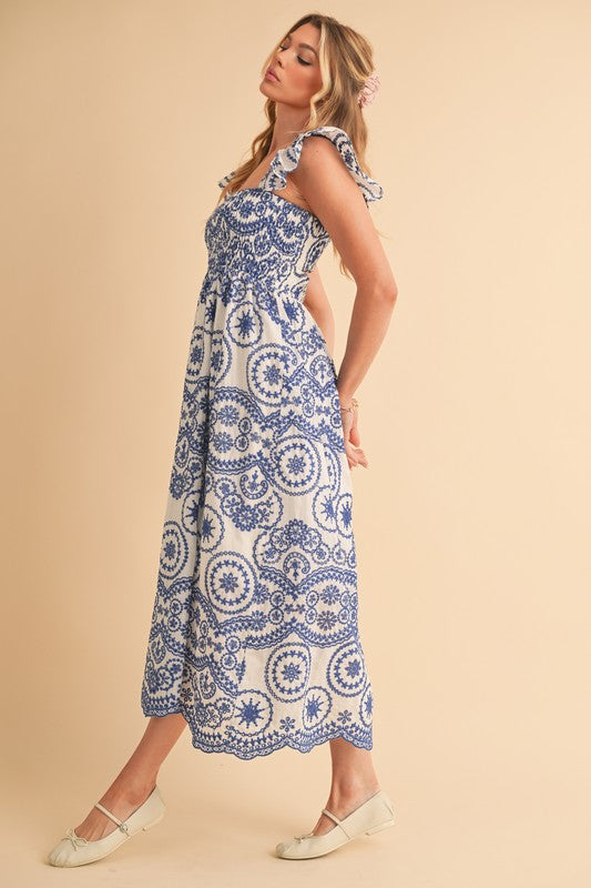The dress is a long, airy maxi with a blue and white geometric/medallion print, cap sleeves, and a fitted bodice that flows into a relaxed, ankle-length skirt.