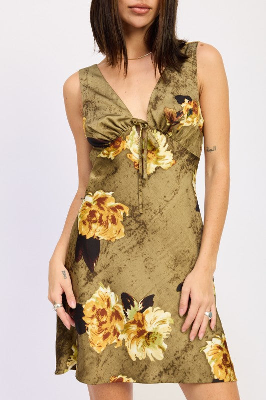 the dress is a short, olive-green floral wrap-style piece with a plunging neckline and a fitted silhouette, featuring large yellow and orange flowers.