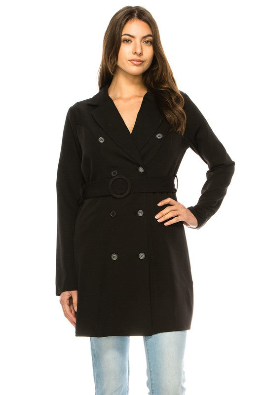A woman wearing a long black coat with big buttons, a white top, and blue jeans. Background's plain white with a black border.