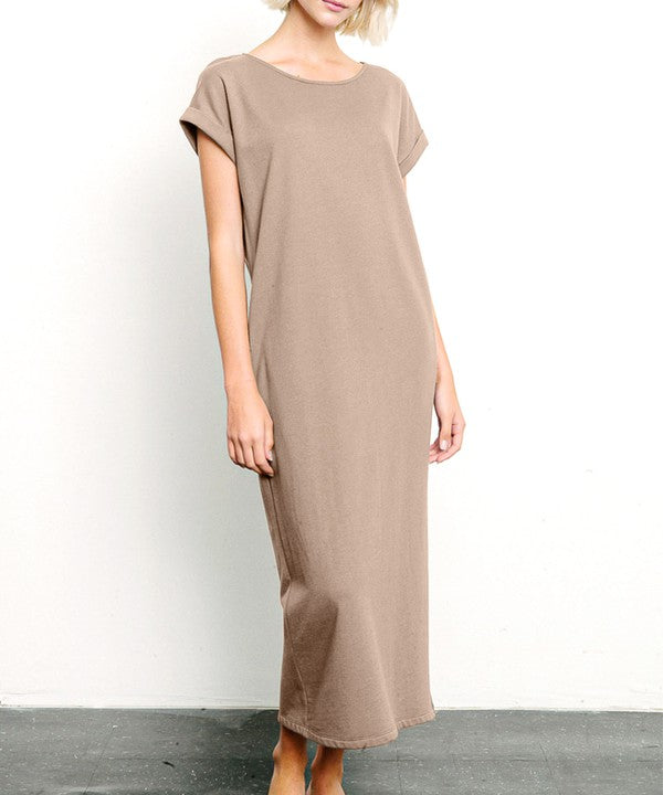 A woman wearing a light pink, short-sleeve, midi-length casual dress with side pockets, paired with black flat sandals.