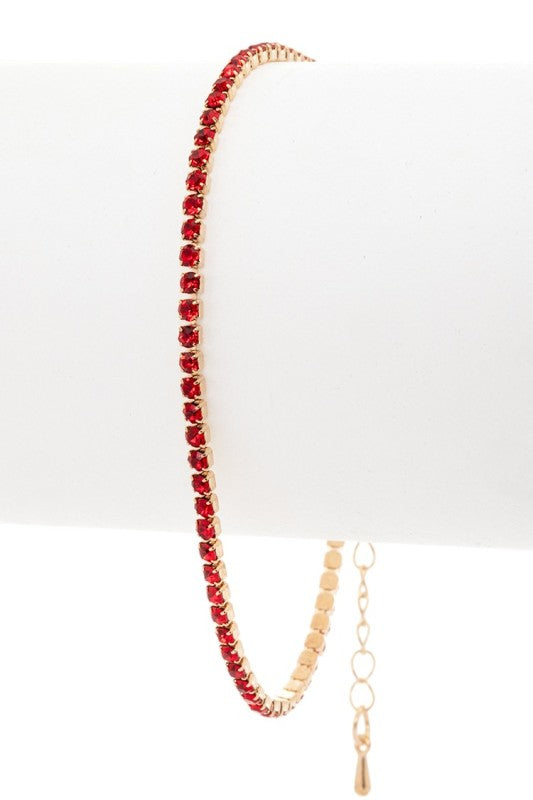 Delicate gold-toned bracelet featuring a continuous row of red gemstones with an adjustable chain and teardrop end, refined, vibrant, and ideal for elegant styling.