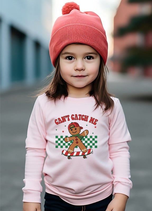 Child wearing a pink sweater with a gingerbread man design and text, standing outdoors.