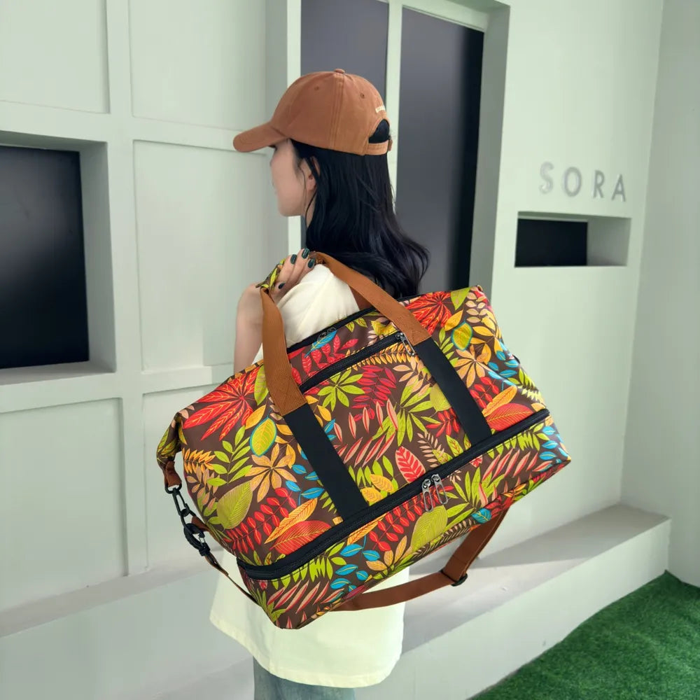 Person standing on a green carpeted floor, holding a colorful duffel bag with a vibrant leaf pattern in red, yellow, green, and blue. They're wearing a white t-shirt with cartoon duck faces and light blue jeans—fun, casual, and eye-catching.