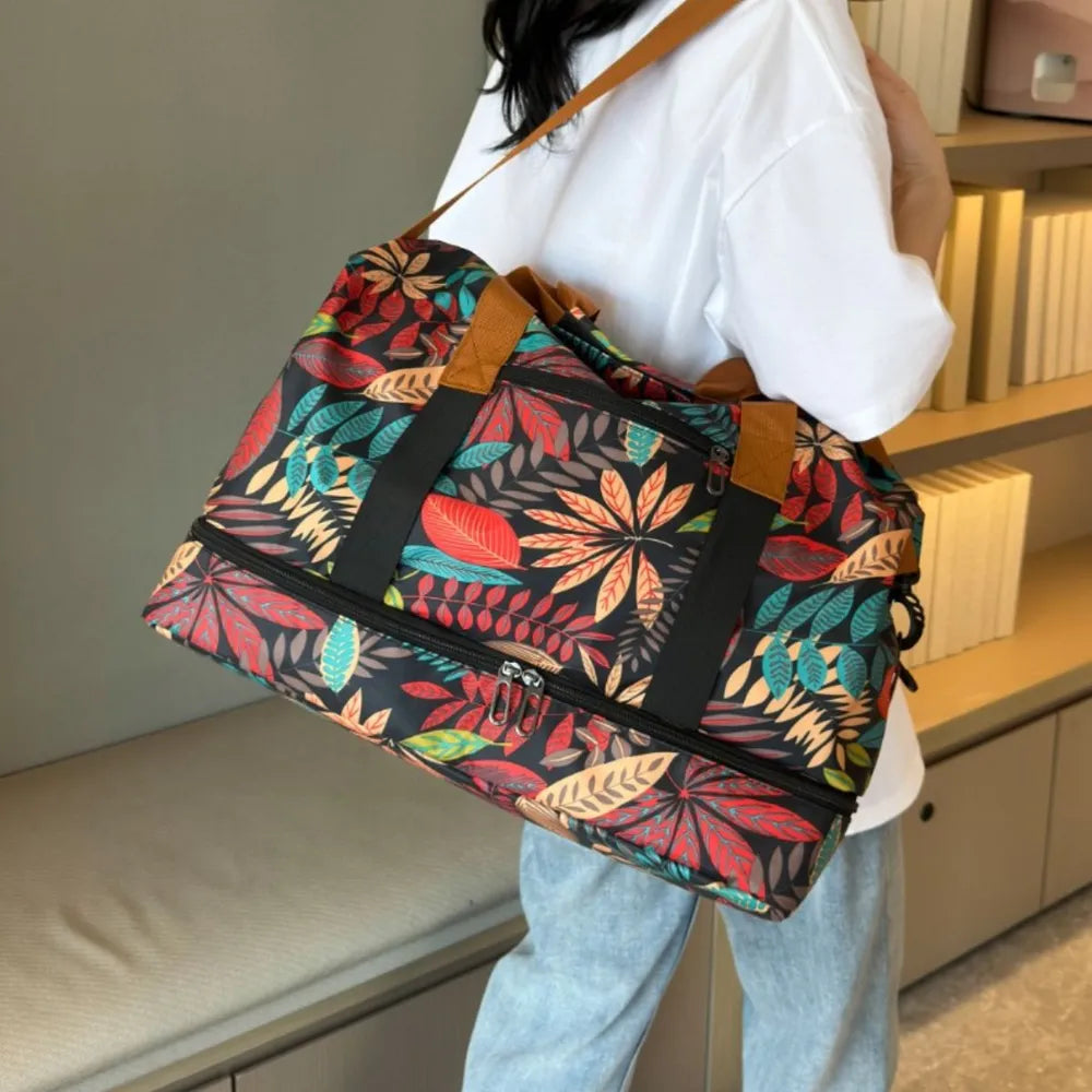 A lady rocking a colorful duffel bag with a vibrant leaf pattern in red, yellow, green, and blue, held by a person wearing a white cartoon t-shirt and light blue jeans. Bold and eye-catching—perfect for travel or casual outings.