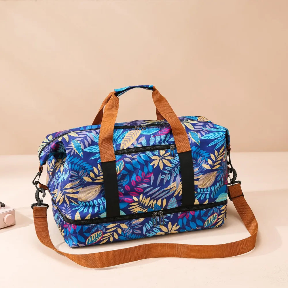 Colorful duffel bag with a bold leaf pattern in blue, yellow, and purple tones, featuring brown handles and a detachable shoulder strap. Eye-catching and tropical—perfect for travel or casual outings.