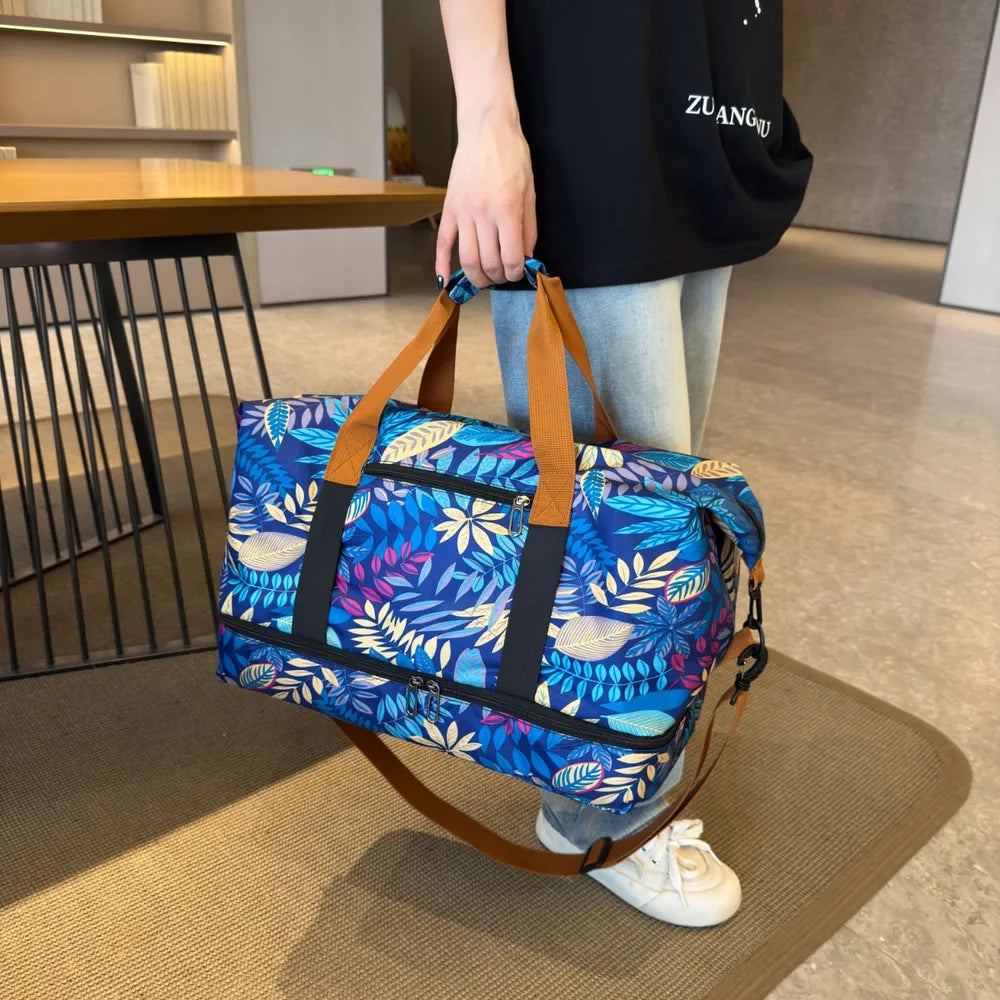 Person holding a vibrant duffel bag with blue, yellow, and green leaf patterns, wearing a black Spanish-text t-shirt and light blue jeans. Stylish and bold—perfect for casual outings or travel.