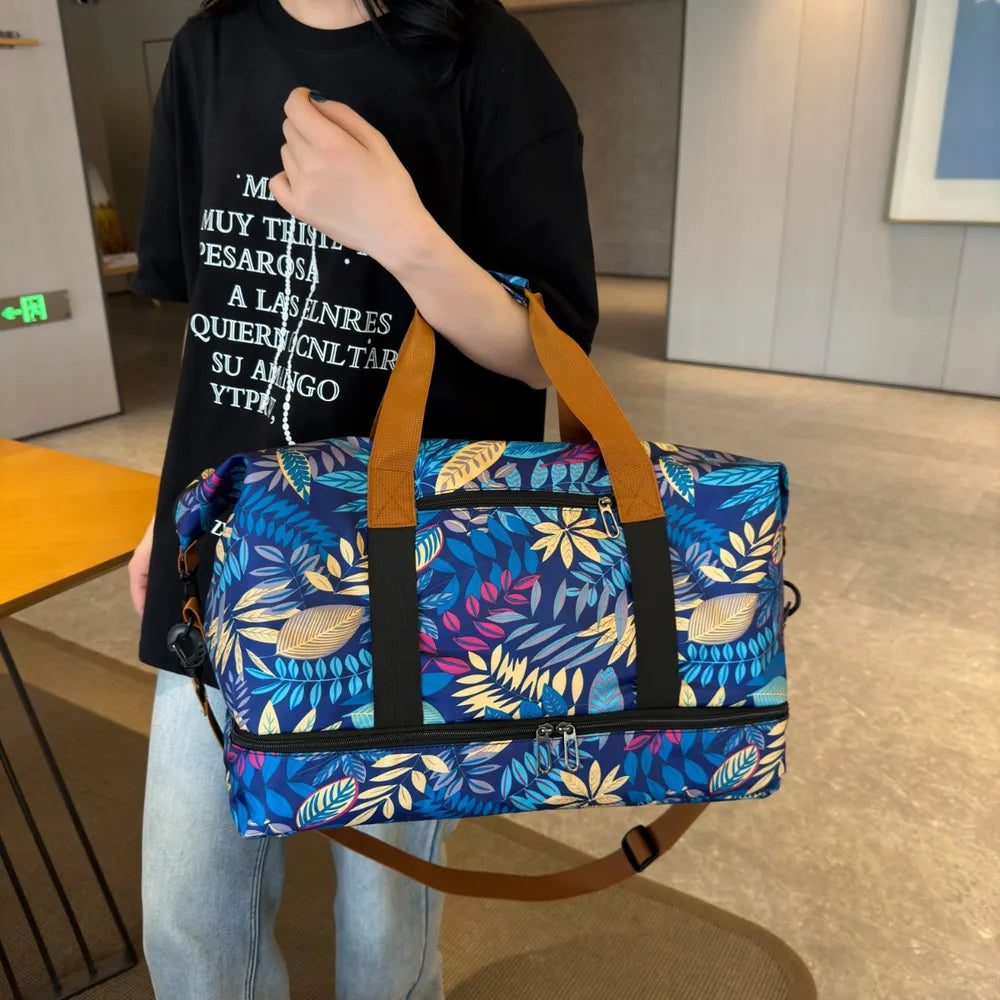 Person holding a vibrant duffel bag with blue, yellow, and green leaf patterns, wearing a black Spanish-text t-shirt and light blue jeans. Stylish and bold—perfect for casual outings or travel.