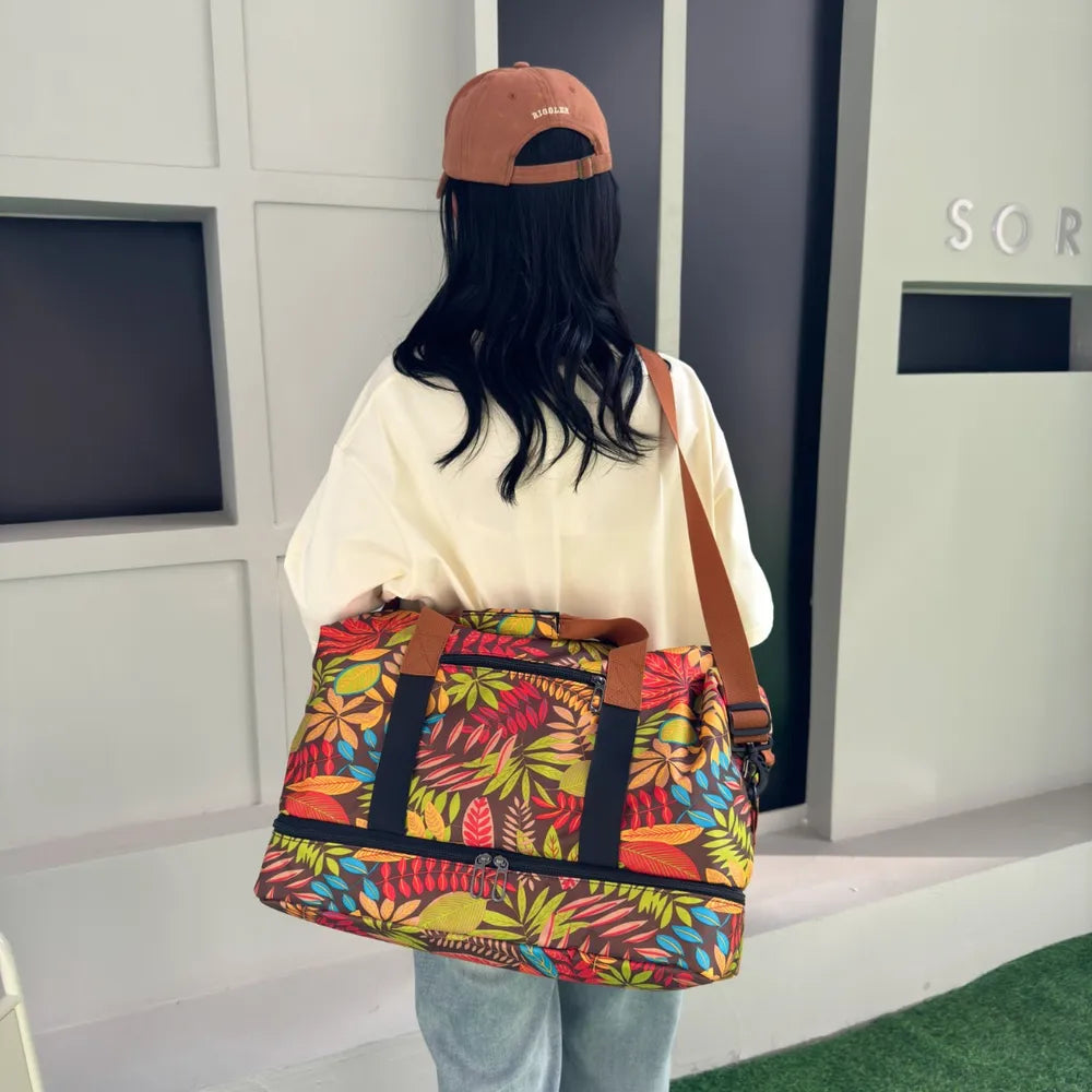 Person standing on a green carpeted floor, holding a colorful duffel bag with a vibrant leaf pattern in red, yellow, green, and blue. They're wearing a white t-shirt with cartoon duck faces and light blue jeans—fun, casual, and eye-catching.