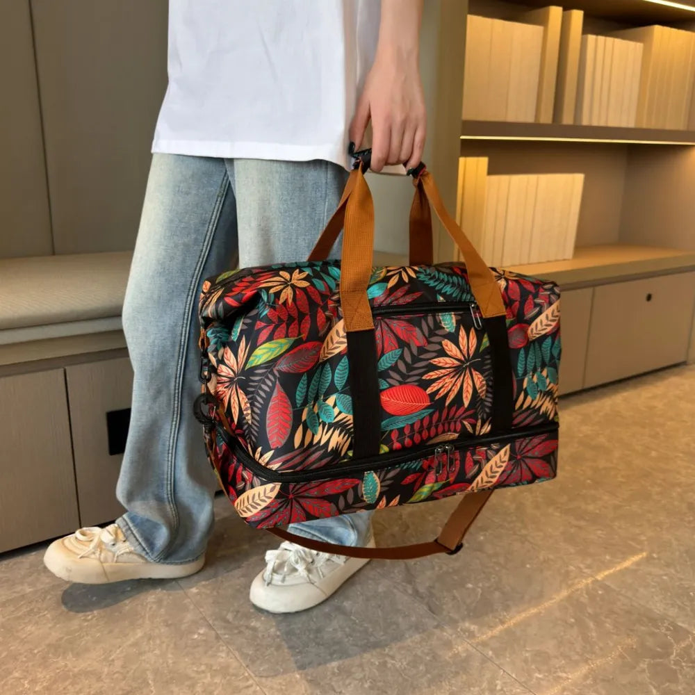 Person holding a colorful duffel bag with a vibrant leaf pattern in red, yellow, green, and blue, held by a person wearing a white cartoon t-shirt and light blue jeans. Bold and eye-catching—perfect for travel or casual outings.