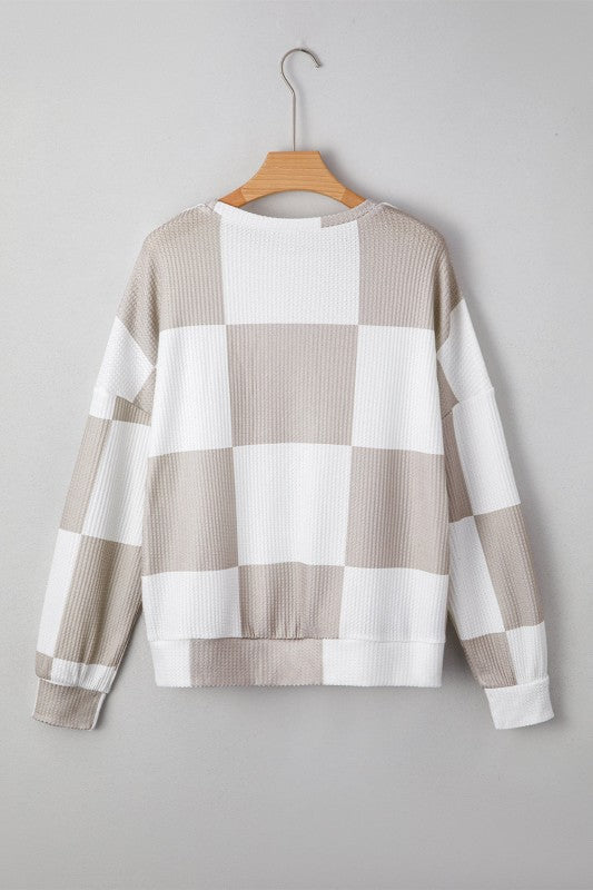 Plaid sweater on a wooden hanger against a gray background
