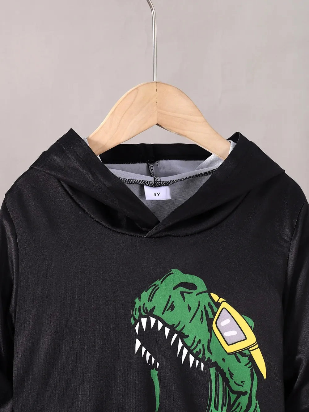 Black hoodie with a green dinosaur graphic on a hanger against a gray background
