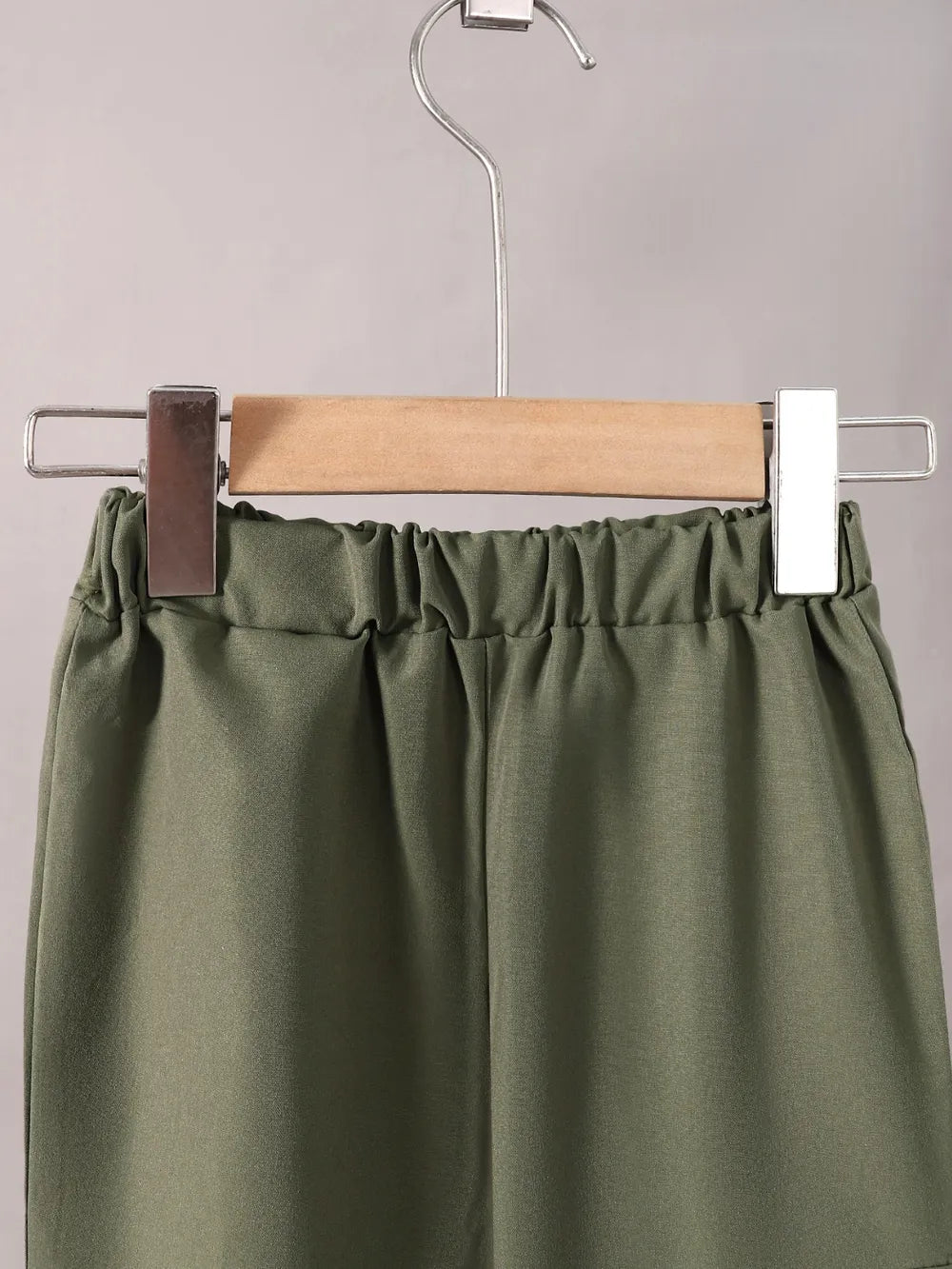 Green pants on a hanger against a gray background