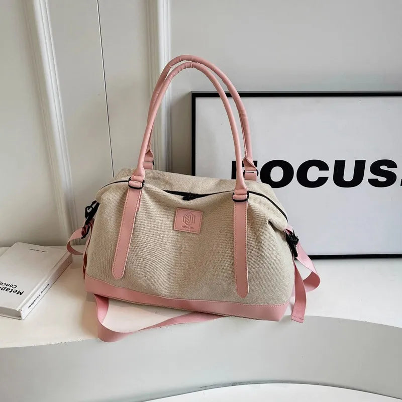 Beige and pink handbag with matching handles, strap, and logo patch—displayed in a minimalist setting.