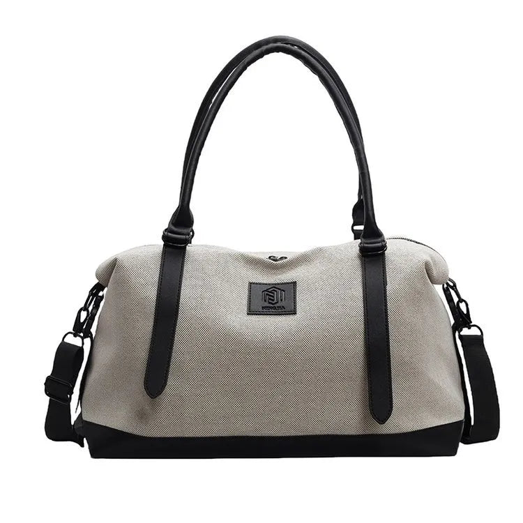 Light beige duffel bag with black handles, bottom, and side straps, featuring a front logo patch—durable, minimalist, and suitable for everyday use.