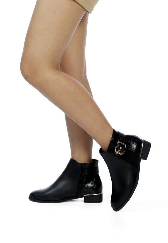 A woman dressed with decorative strap with a gold-tone buckle runs around the outer side near the ankle.