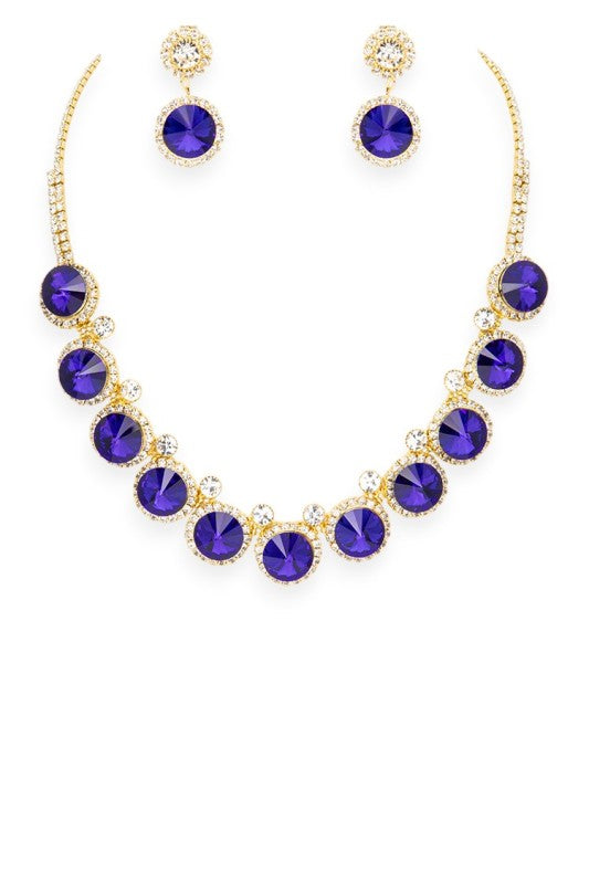 Gold-toned jewelry set featuring a necklace and matching earrings, each adorned with deep blue gemstones encircled by clear stones, elegant, radiant, and ideal for formal occasions.
