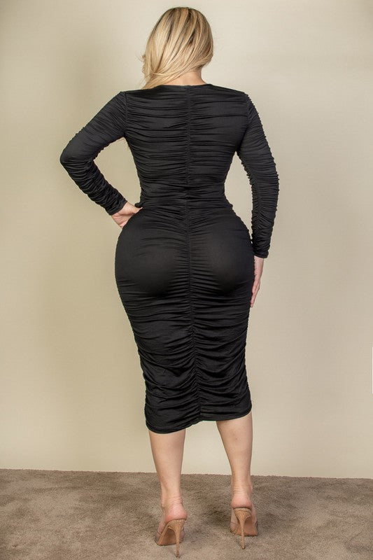 A woman wearing a flattering black ruched midi dress with long sleeves and a V-neck, showcasing elegant texture.