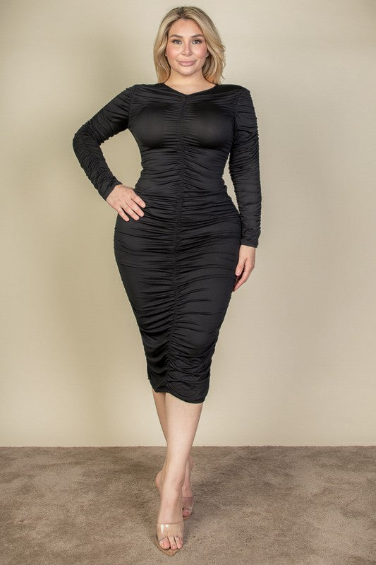 A woman wearing a flattering black ruched midi dress with long sleeves and a V-neck, showcasing elegant texture, and posing stylishly.