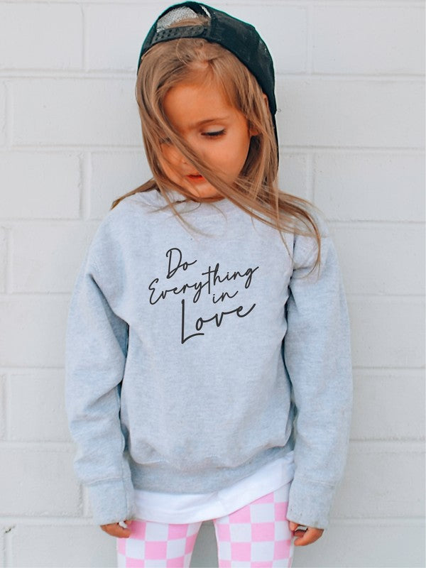 Child wearing a gray sweatshirt with 'Do Everything in Love' text against a white brick wall.
