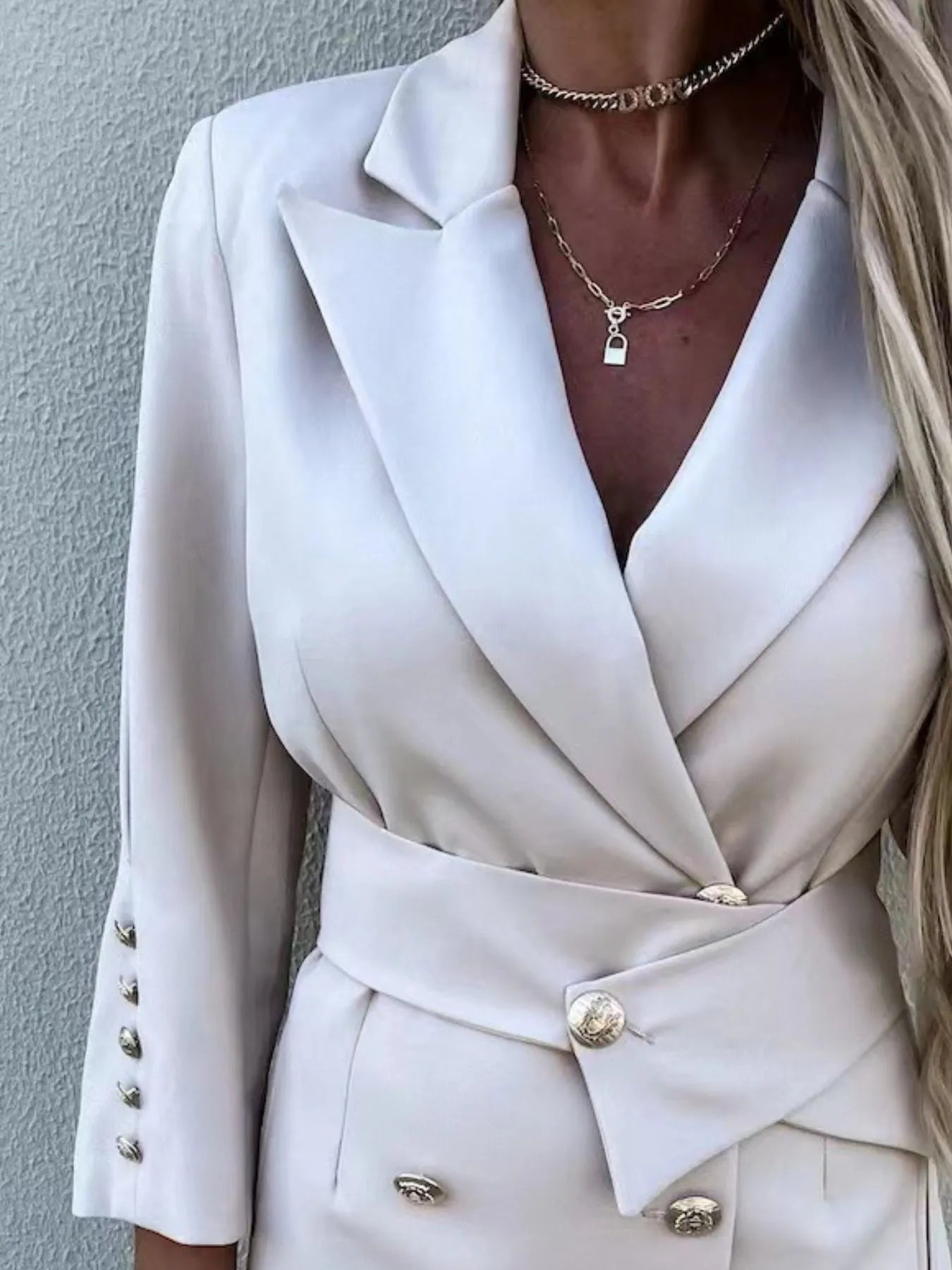 A woman in a stylish white double-breasted blazer dress with gold buttons, accessorized with jewelry and a clutch.
