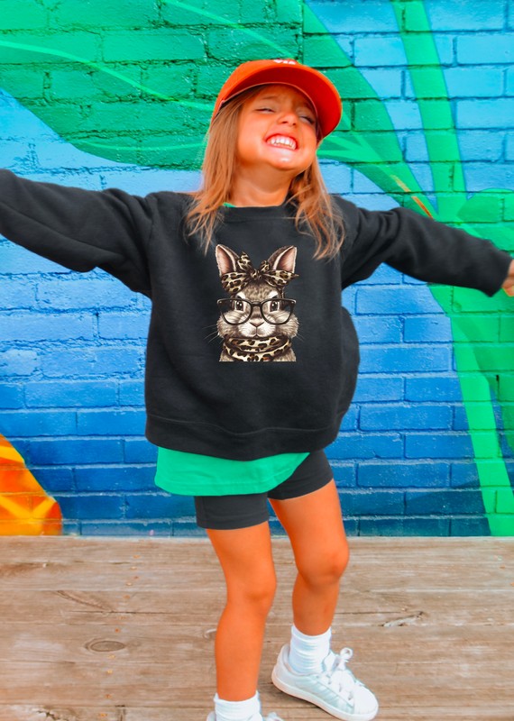 A kid wearing a black sweatshirt with a graphic design, green shorts, and white sneakers