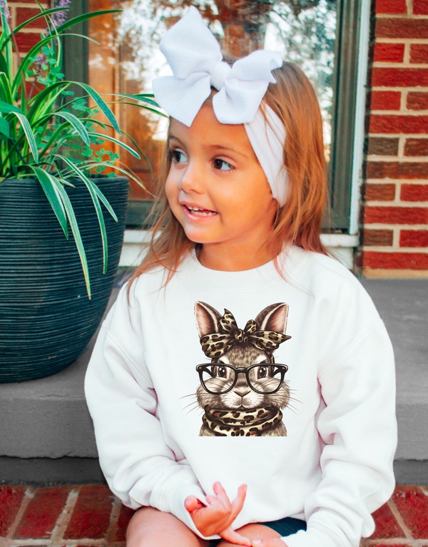 Child wearing a white sweatshirt with a cat graphic, sitting outdoors.