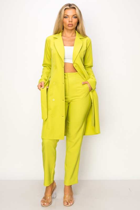 A woman wearing a bright yellow-green coat with a belt and matching pants. She's standing against a white background with her hands in the coat's pockets.