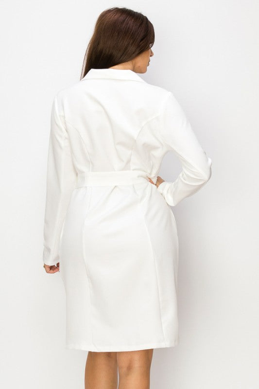 A woman wearing a crisp white belted coat dress with long sleeves and a collar. She's posing with one hand in her pocket and the other by her side, against a plain white background.