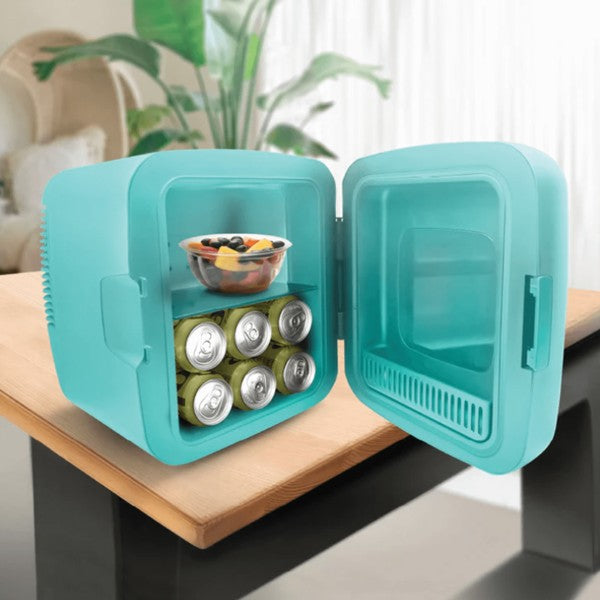 Open turquoise mini fridge on a black-base wooden table, containing six cans and a fruit salad—set in a cozy room with plants, curtains, and an armchair in the background.