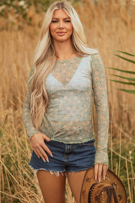 Lady in a sheer green floral top and frayed denim shorts, holding a straw hat, effortless, breezy style perfect for sunny outdoor days.