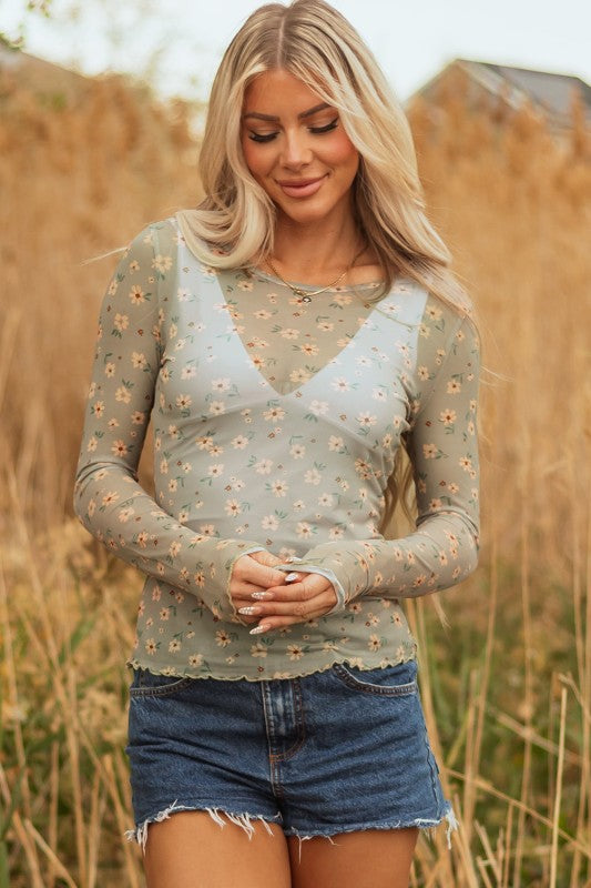 Lady in a sheer green floral top and frayed denim shorts, breezy style perfect for sunny outdoor days.