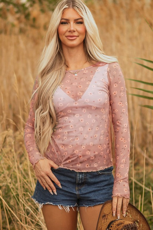 Lady in a sheer pink floral top and frayed denim shorts, holding a straw hat, effortless, breezy style perfect for sunny outdoor days.
