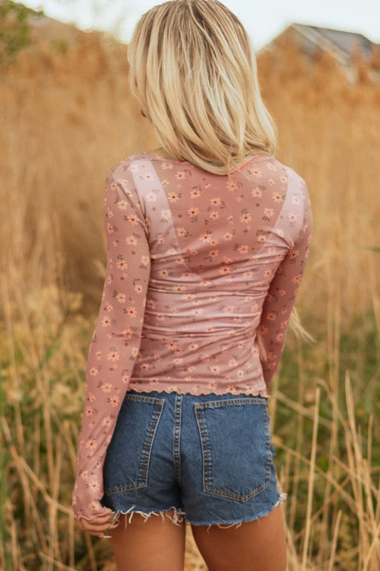 Lady in a sheer pink floral top and frayed denim shorts, holding a straw hat, effortless, breezy style perfect for sunny outdoor days.