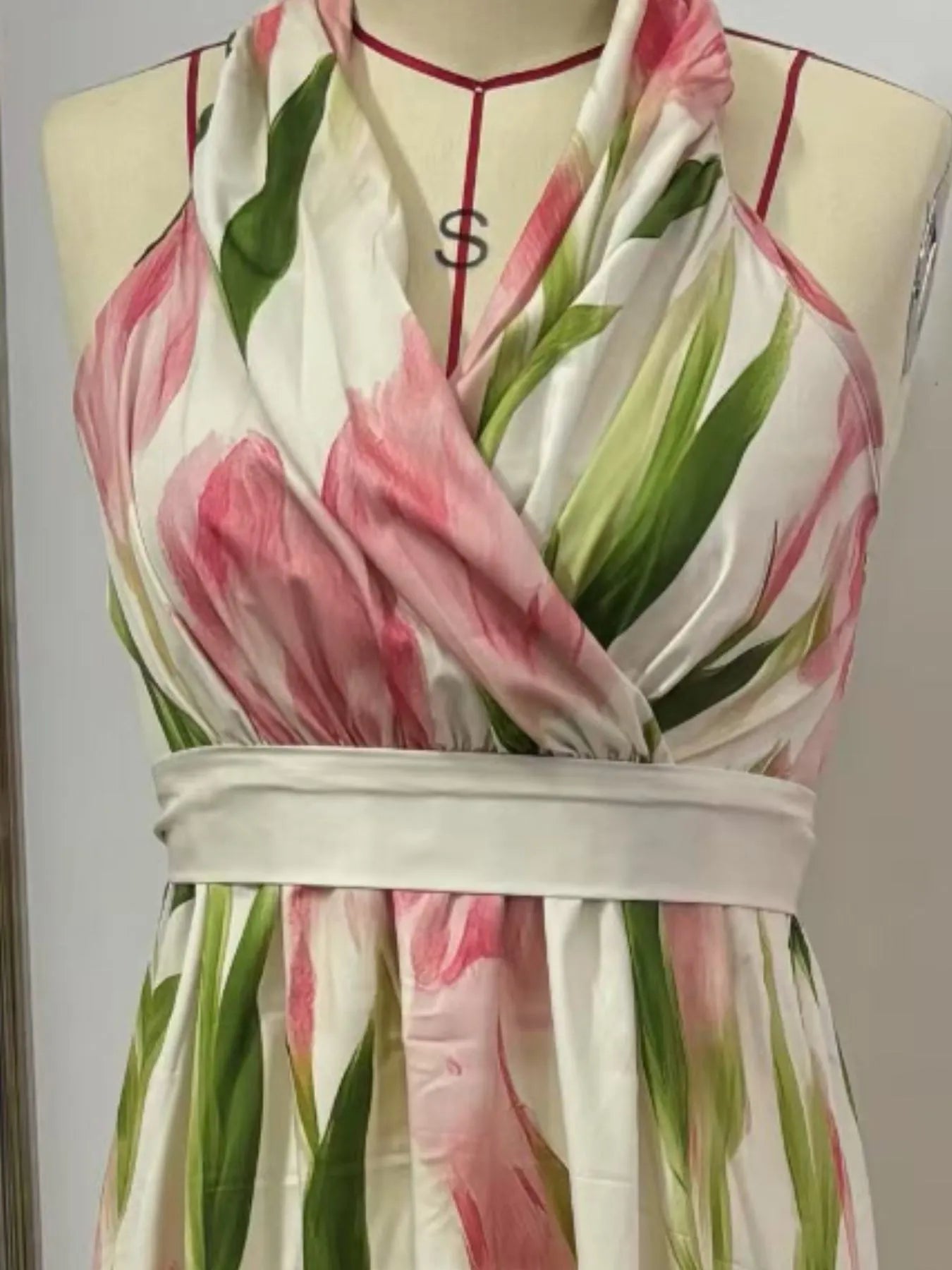 A flowy, white maxi dress with pink flowers and green leaves. It's a halter neck dress with a V-neckline and a belt at the waist.