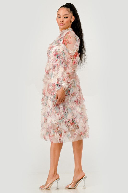 A woman wearing a Floral Ruffle Sheer Midi Dress, features an all over pastel floral print with cascading ruffle detailing for a soft, textured finish, side view.