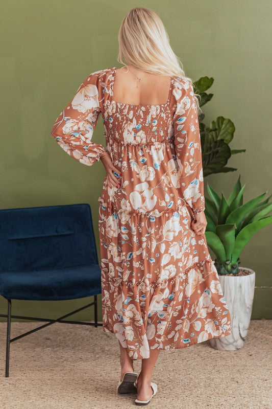 Woman wearing a floral dress standing in a room with a green wall and plant.
