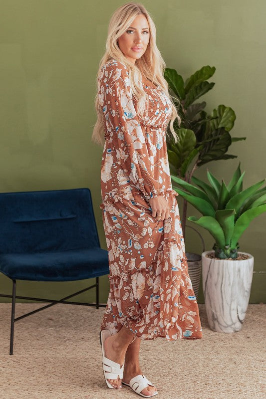 Woman in a floral dress standing in a room with a green wall, blue chair, and potted plants.