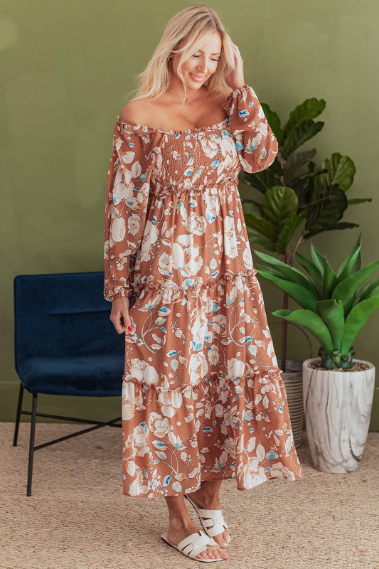 Woman wearing a floral off-shoulder dress in a room with plants and a chair.