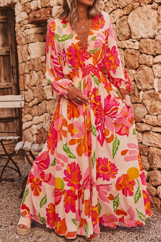 A woman wearing a flowy maxi dress with a vibrant floral print in pink, orange, and green.
