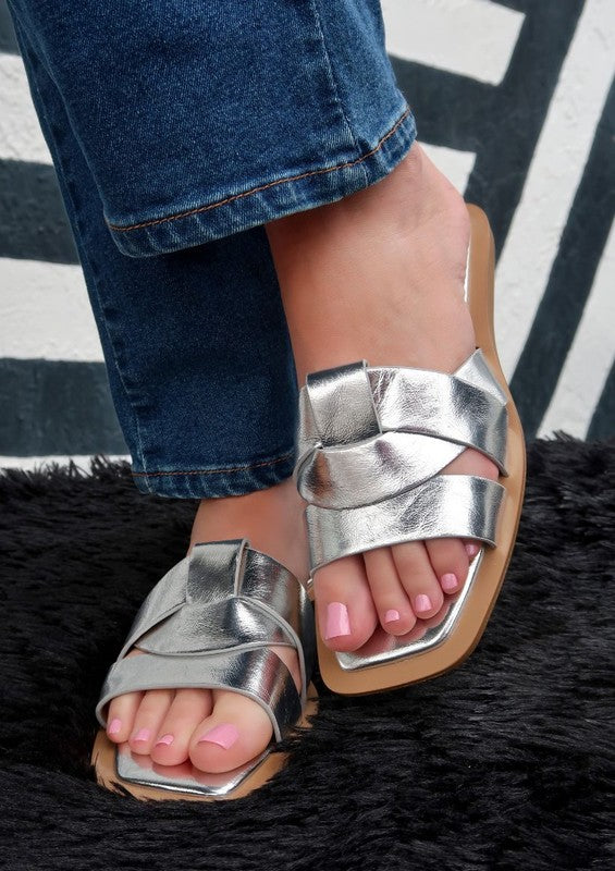 Slip-on sandals featuring woven metallic leather straps, open-toe silhouette, and contoured footbed with flat sole