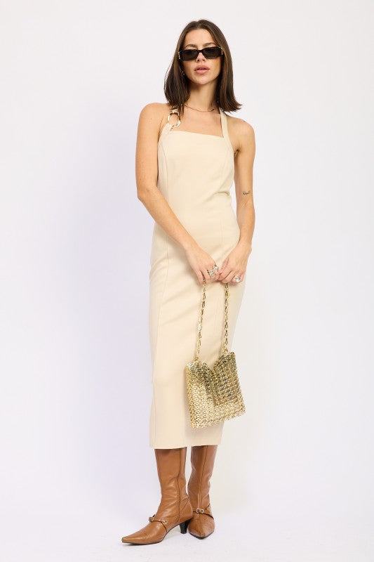 Woman models a chic halter neck midi dress in a neutral cream color, featuring a fitted silhouette and elegant design, posing stylishly.