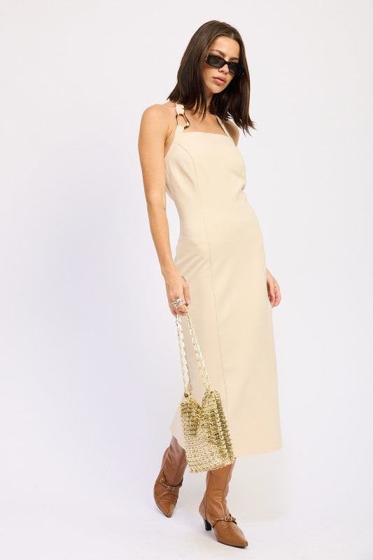 Woman models a chic halter neck midi dress in a neutral cream color, featuring a fitted silhouette and elegant design, in motion.